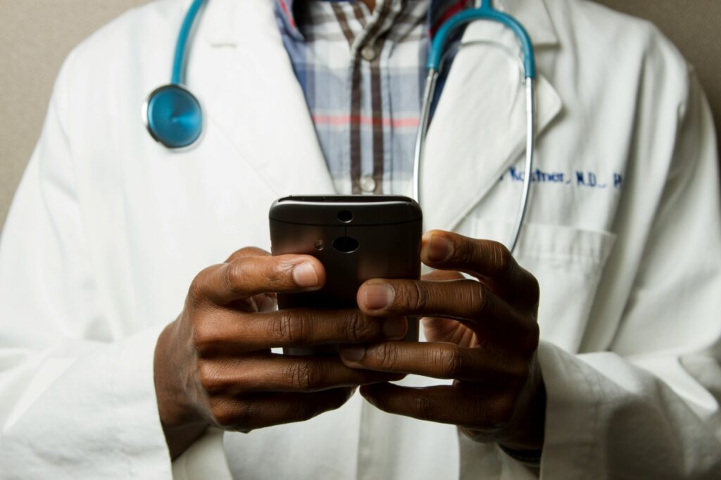 Doctor with a stethoscope around his neck using a smart phone.