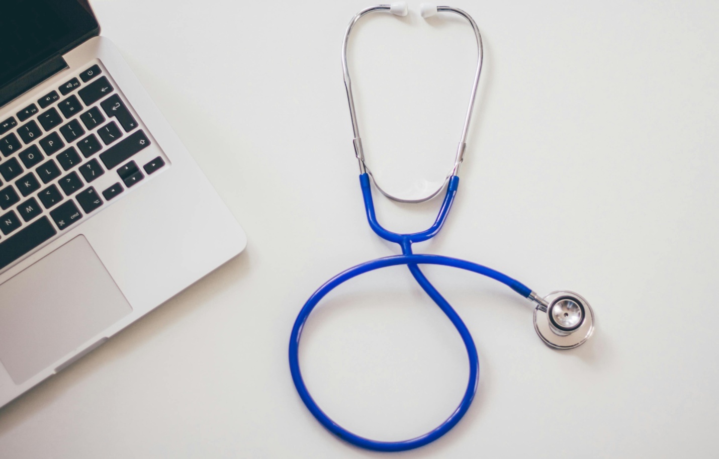 A laptop and blue stethoscope on a computer table.