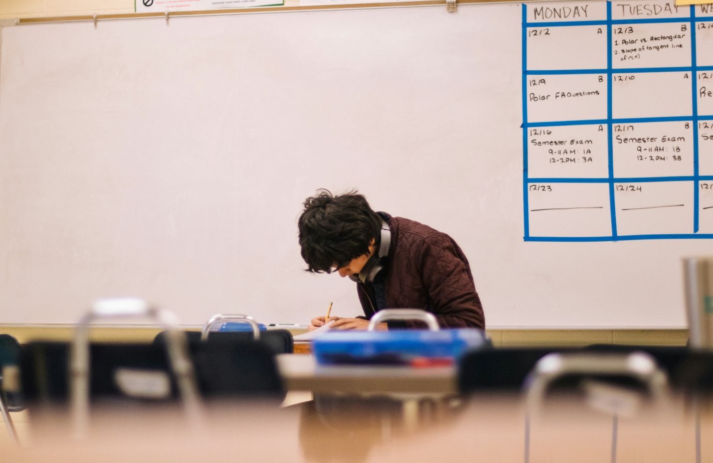 Student wearing a brown sweater working in a classroom.