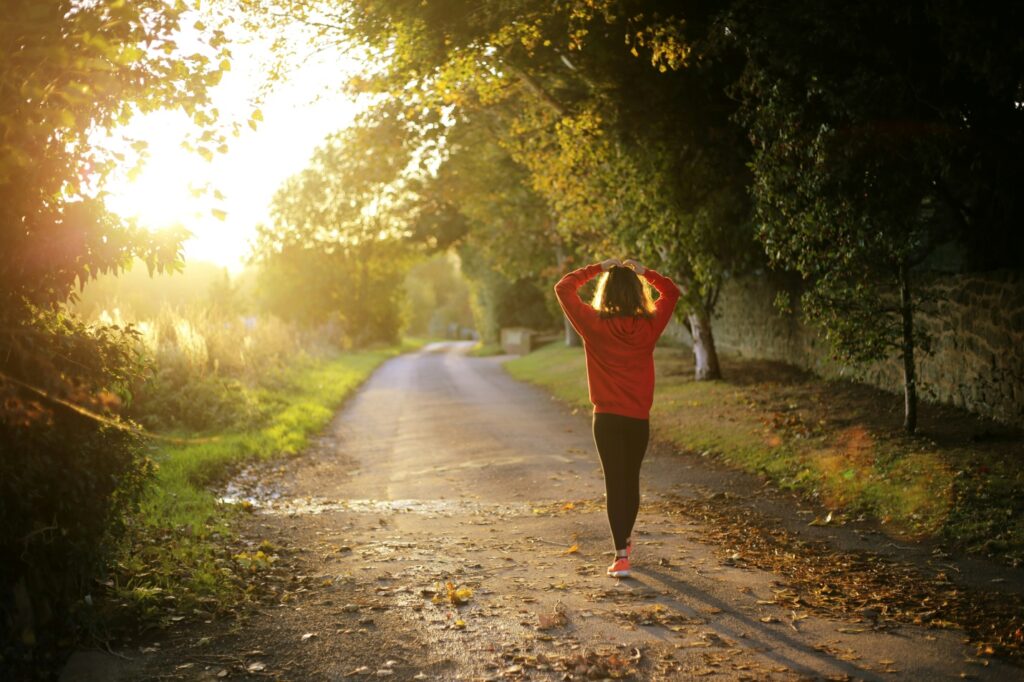 Woman wearing a red shirt surrounded by trees in the morning sun.