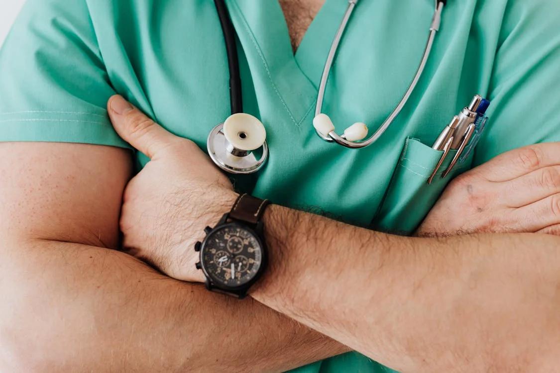 A doctor wearing a stethoscope around his neck with his arms crossed around his chest