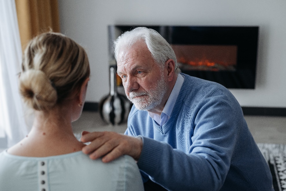 An elderly man consoling a woman wearing a bun on her head