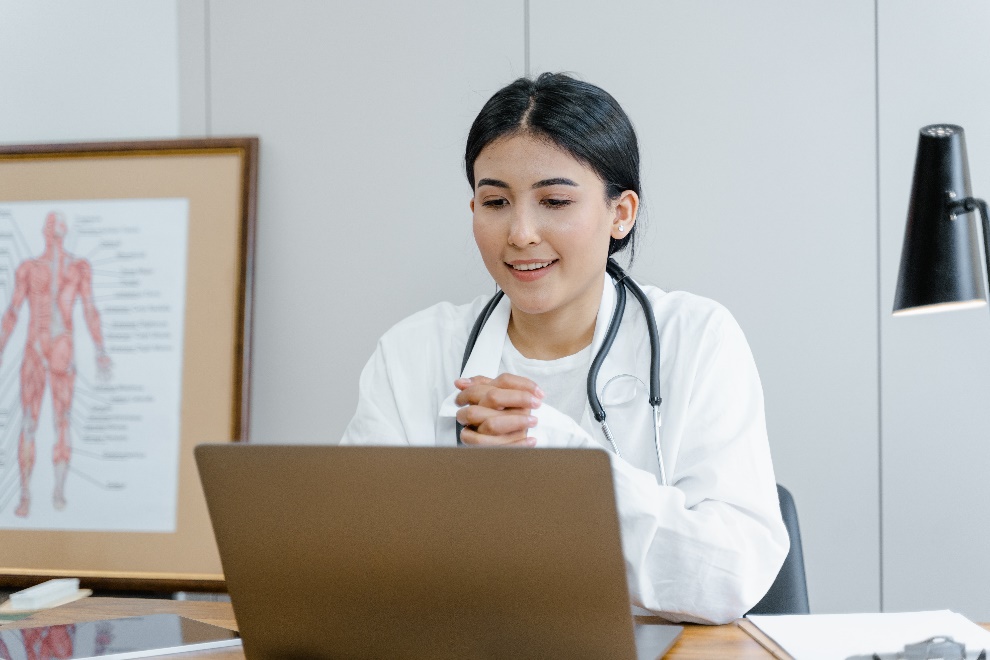  A young doctor wearing a stethoscope looking at her laptop while smiling