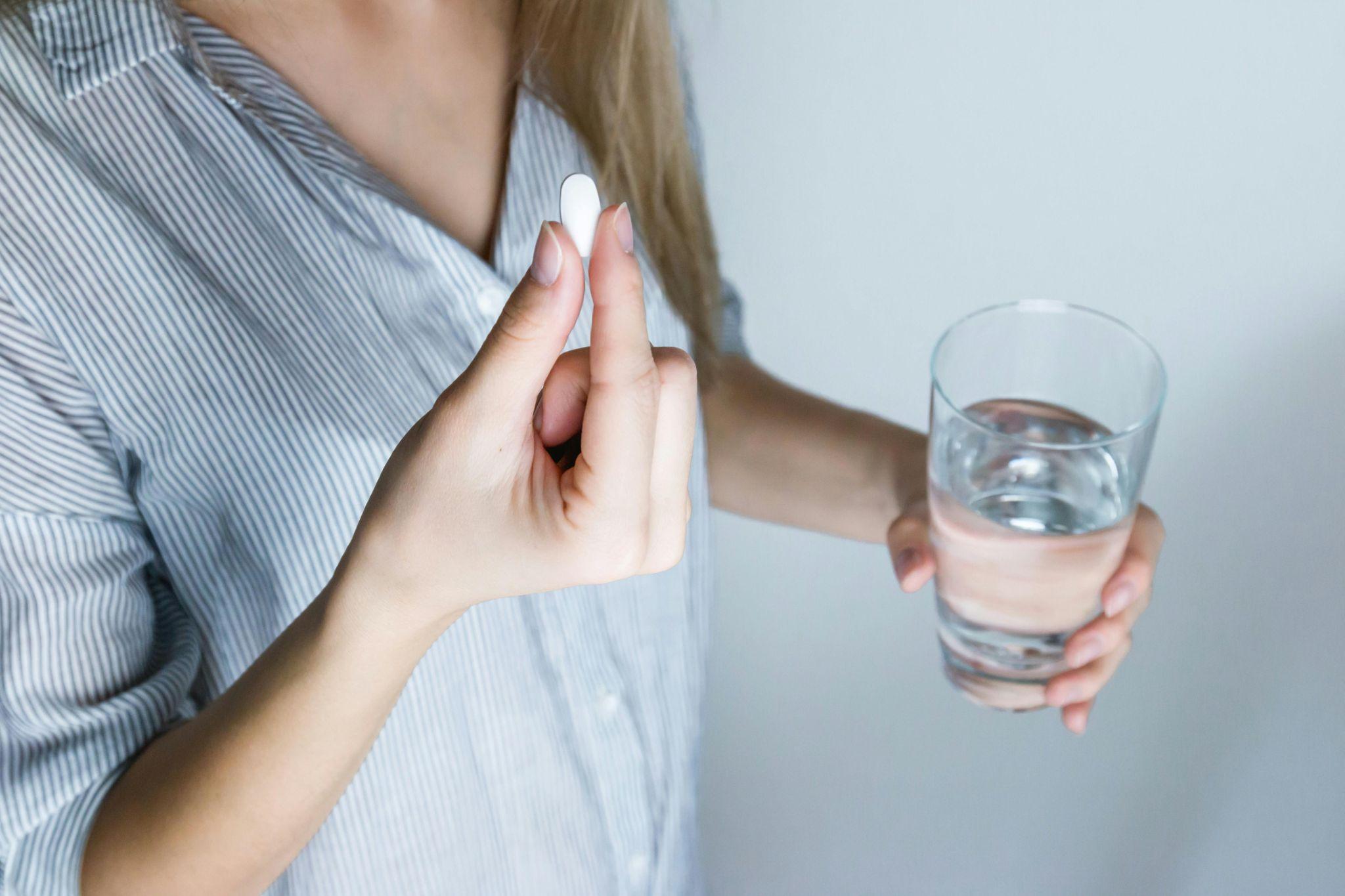 A woman holding a pill and a glass of water