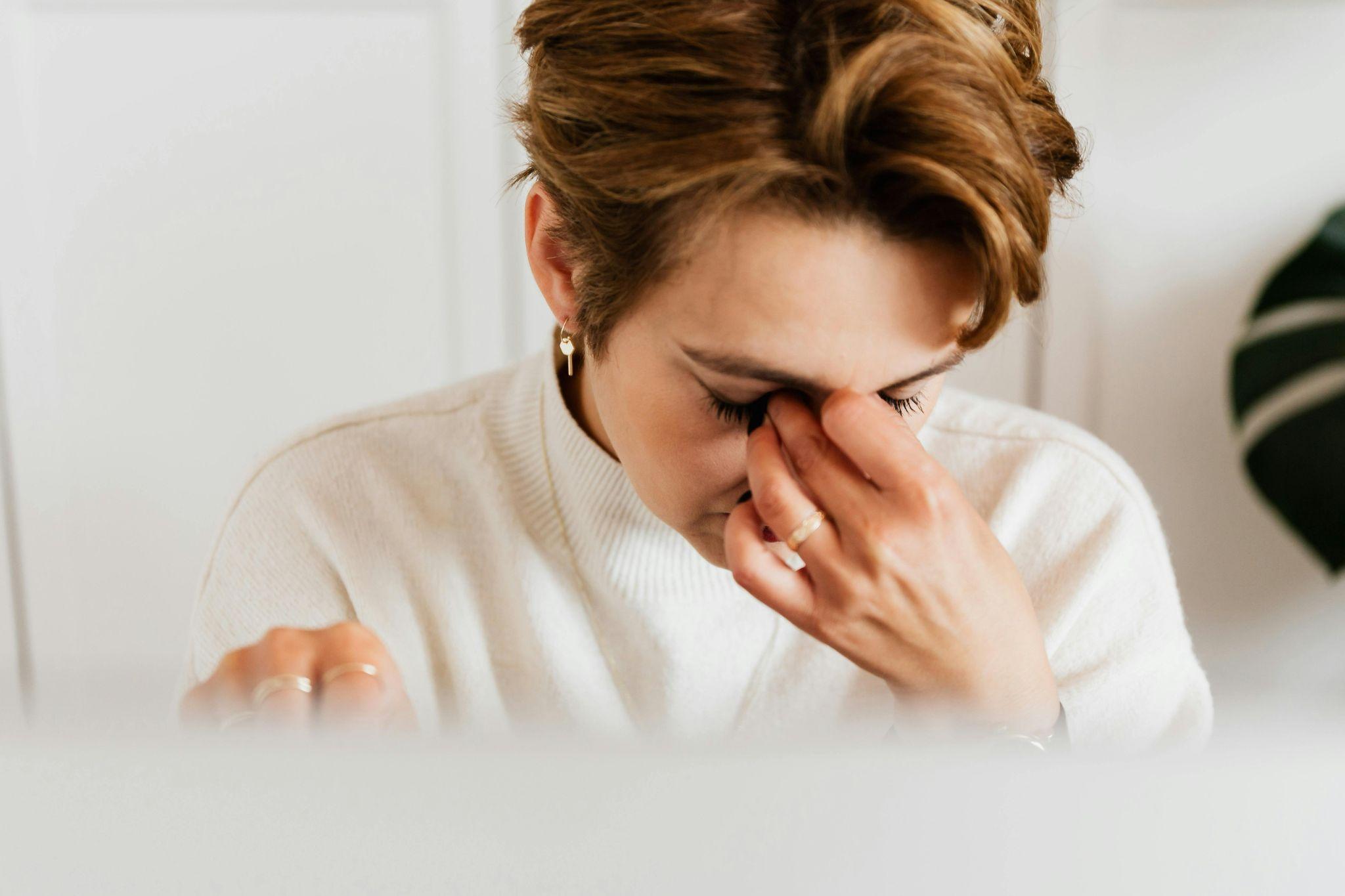 A woman is feeling dizzy and rubbing her eyes due to anemia.