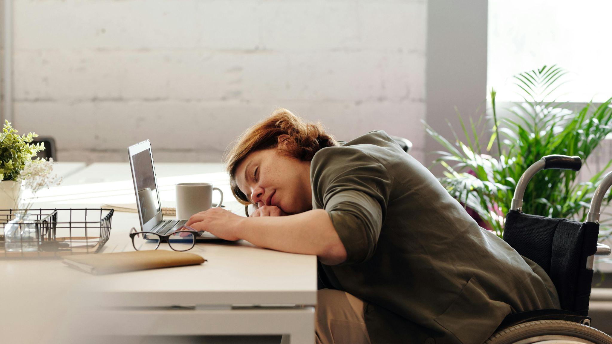 A woman is asleep on her desk due to extreme fatigue.