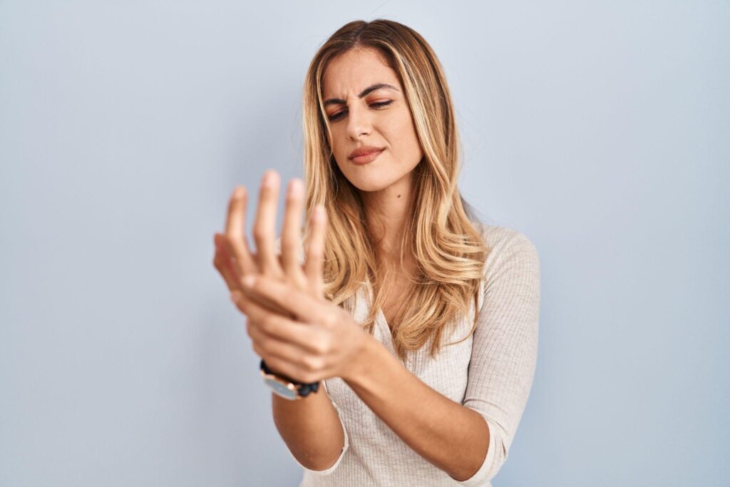 A woman holding her fingers and knuckles in pain due to arthritis.