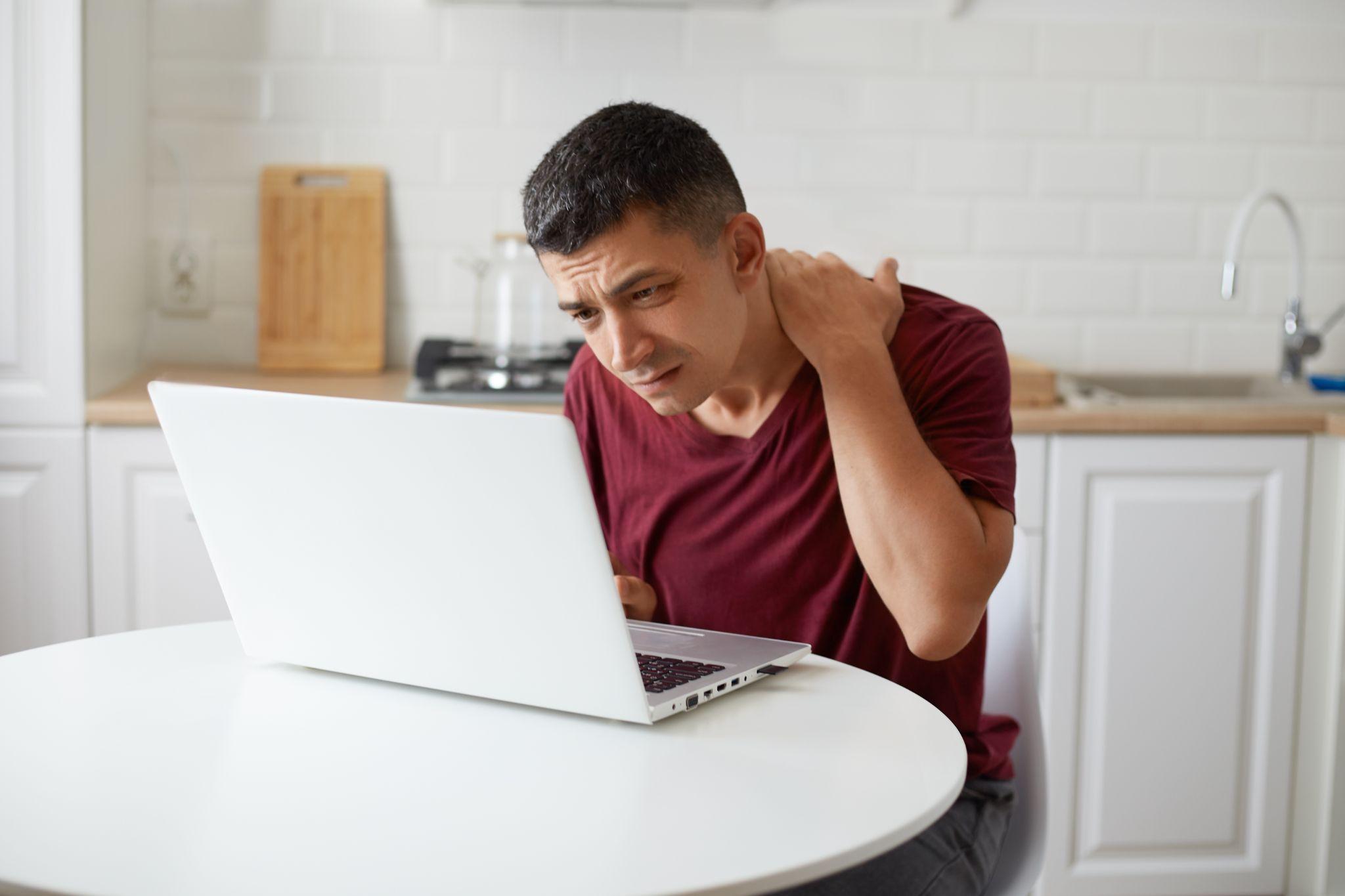 A man experiencing shoulder pain while working on his laptop.