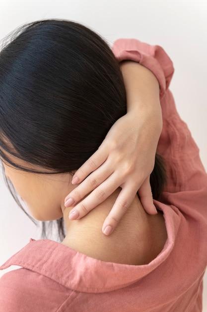 A rear view of a woman holding her upper back in discomfort, representing back pain and muscle tension.