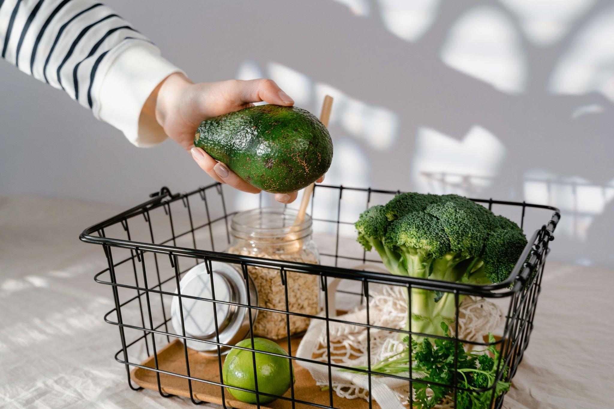 A person placing fresh vegetables and fruits into a shopping basket.