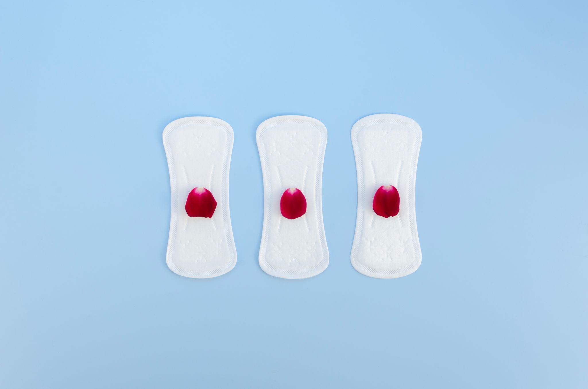 Sanitary pads arranged with flower petals on a blue background.
