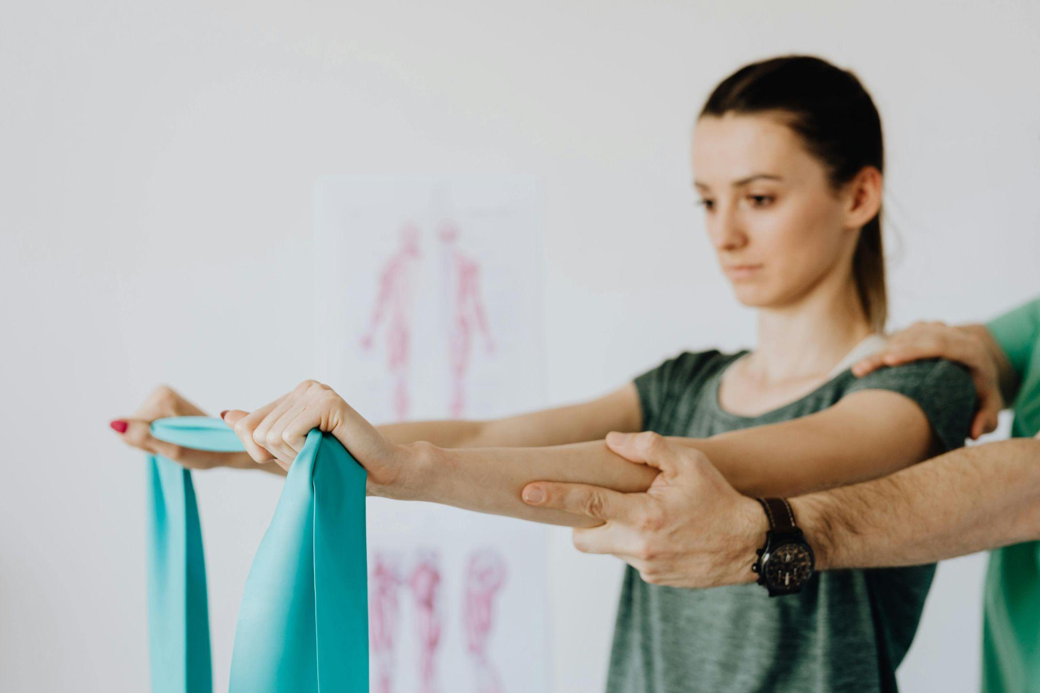 A physical therapist guiding a woman through a resistance band exercise.