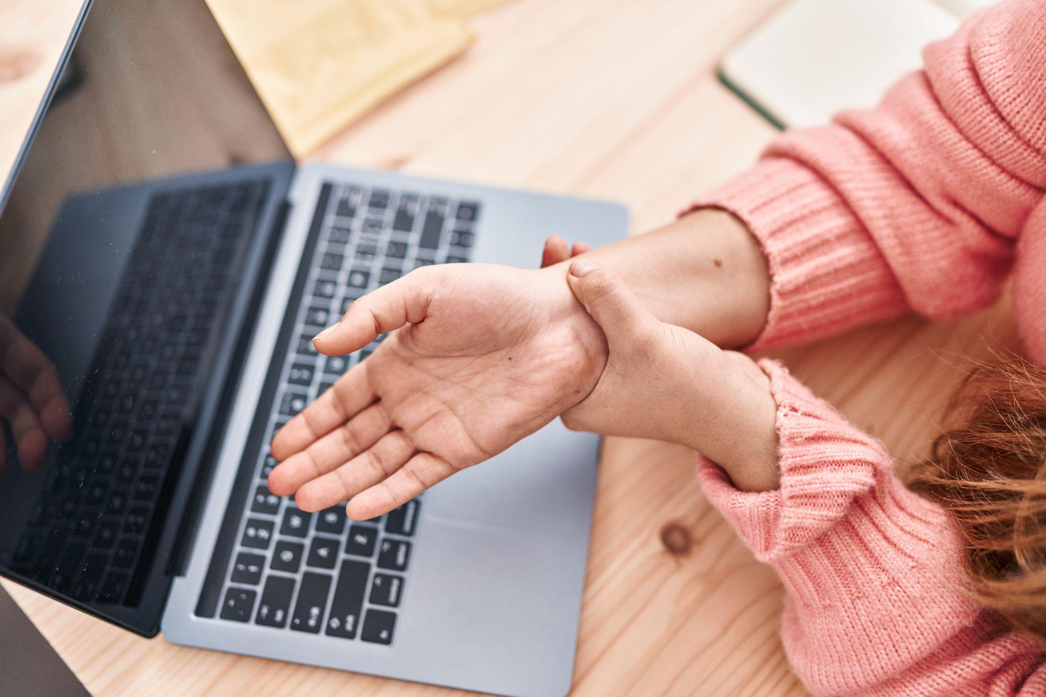 Woman holding her painful hand in front of a laptop