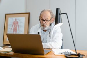 Elderly doctor sitting Infront of his laptop