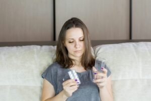 Woman holding water and medication to manage fever responsibly without overmedication while aiming to reduce high fever.