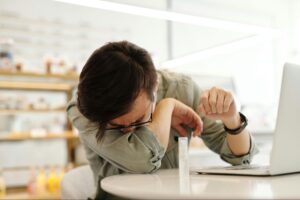 A man sneezing while sitting at a desk with a laptop