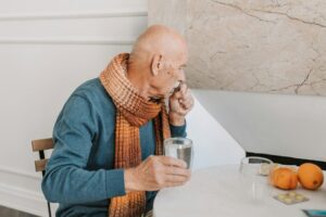 Elderly man sitting at a table, coughing while holding a glass of water