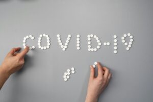 Hands arranging white pills to spell the word COVID-19 on a gray background