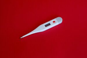 Digital thermometer placed on a red background showing the fever indicator