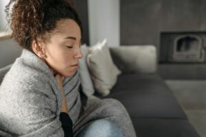 Woman wrapped in a blanket, holding her throat while feeling sick