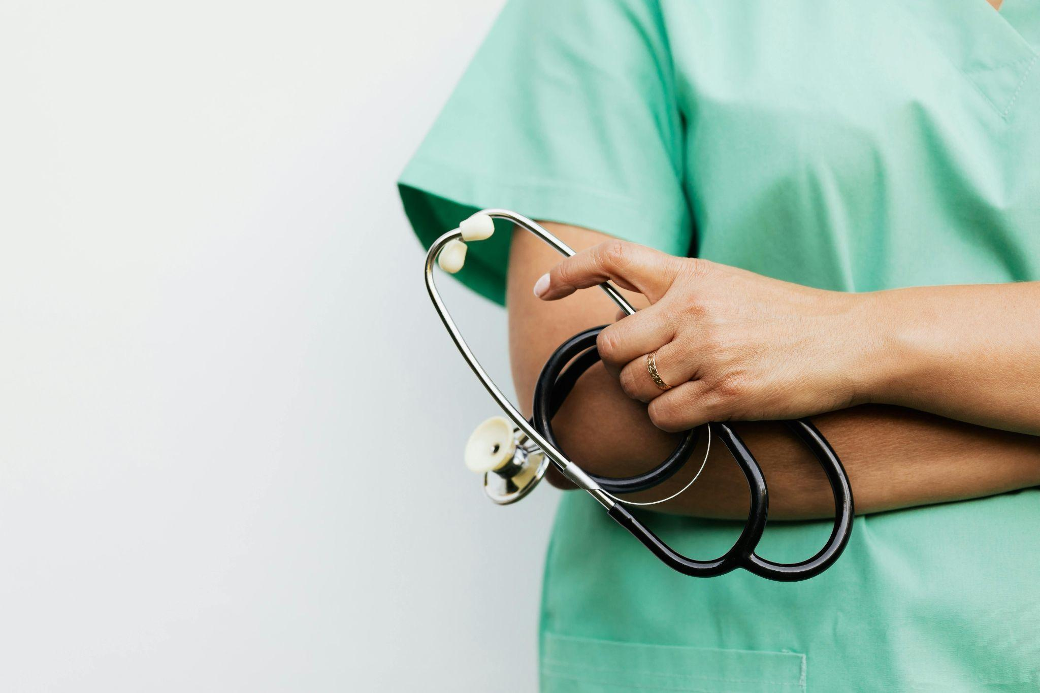 Medical professional holding a stethoscope against green scrubs.