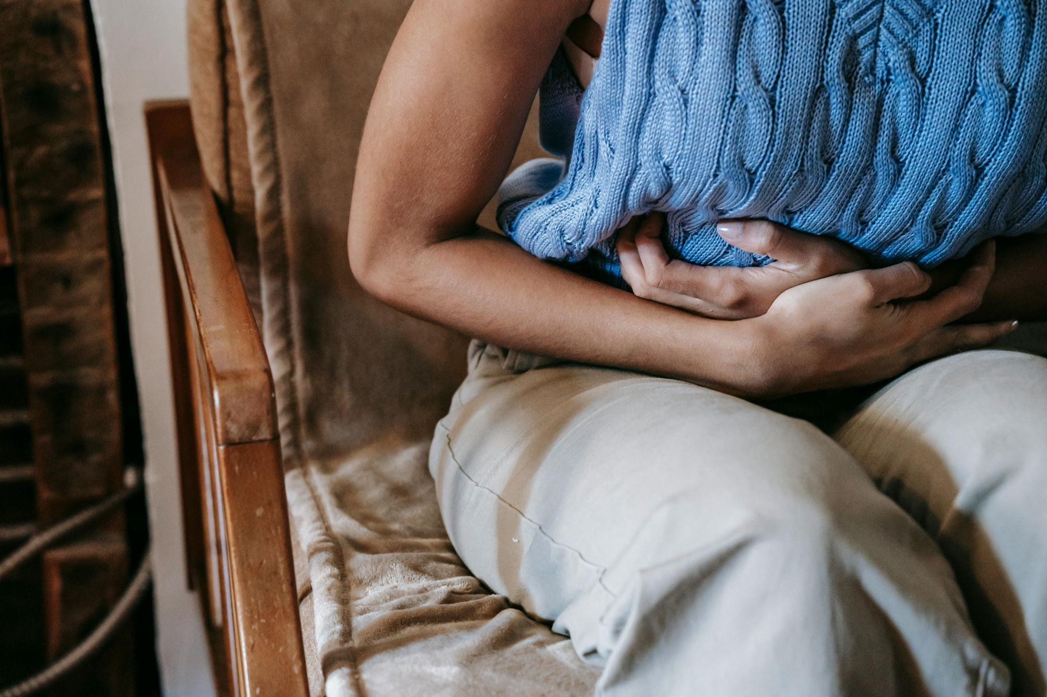 person clutching stomach while seated, indicating abdominal discomfort