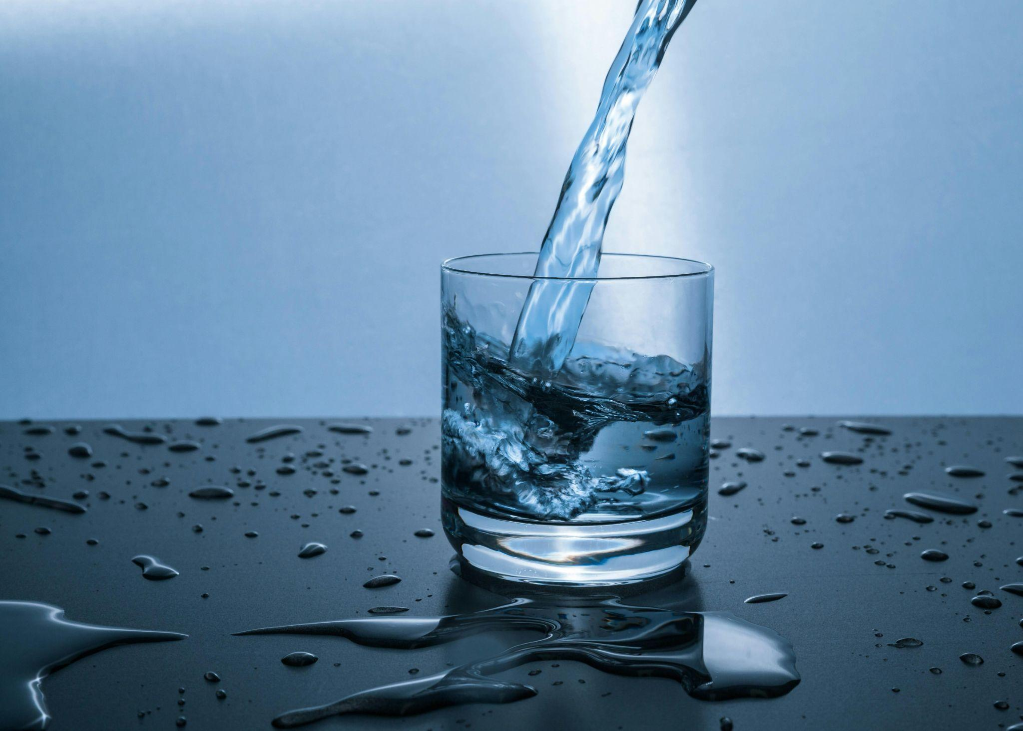 Water being poured into a glass on a reflective surface.
