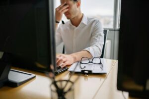 Office worker holding his head while sitting at a computer.