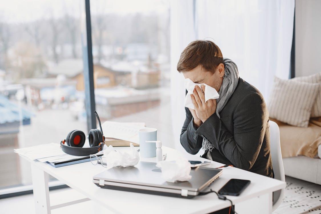 Adult sitting at home office desk blowing nose with tissues