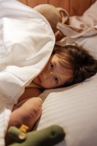 a child lying in bed with plush toys.