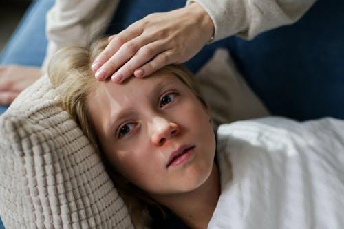 Child lying on a couch while a parent checks for fever