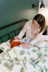 a woman tucking her child in bed. 
