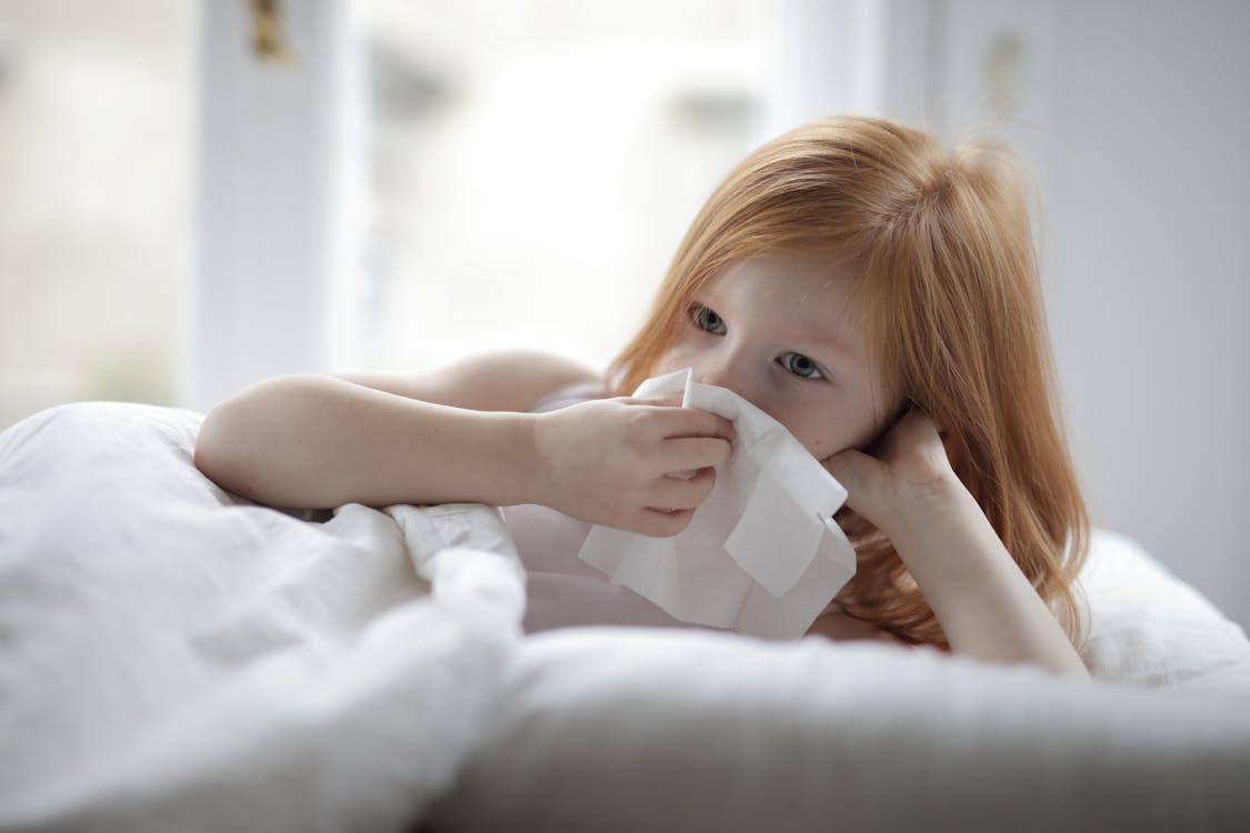 Child lying in bed using a tissue while sick at home during a school absence.