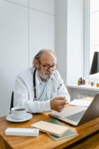 An elderly doctor conducting a video conference using a laptop in a modern office