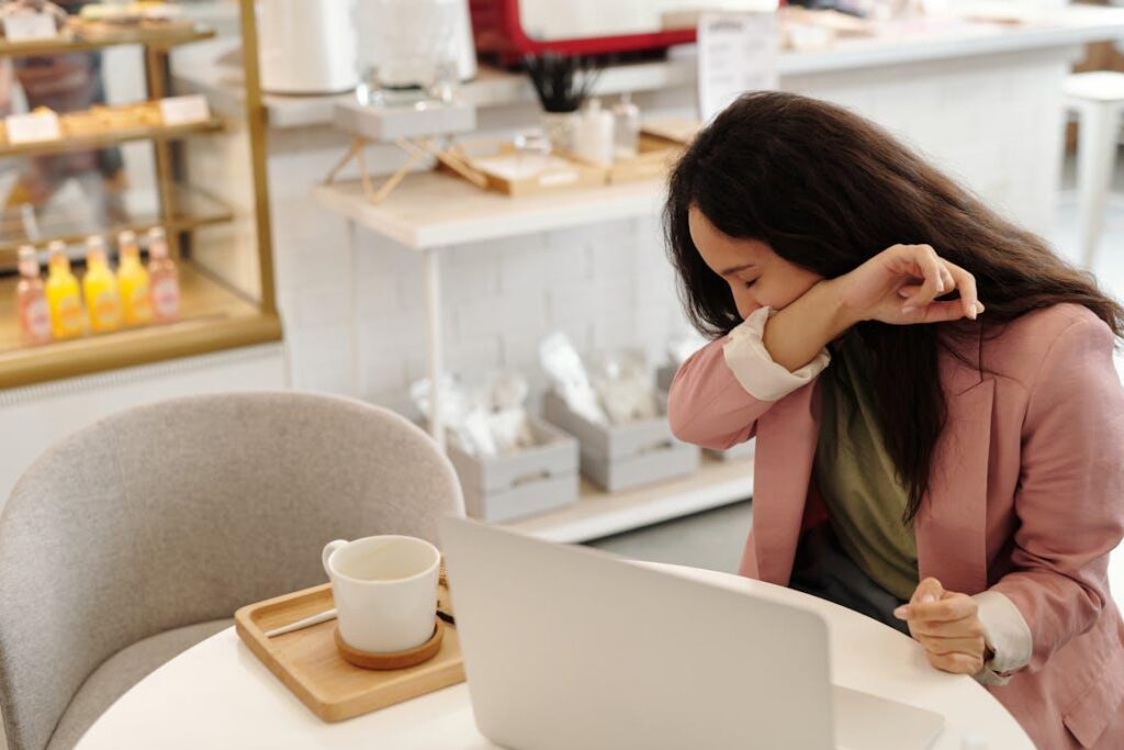 a sick person covering her mouth while sneezing near the laptop