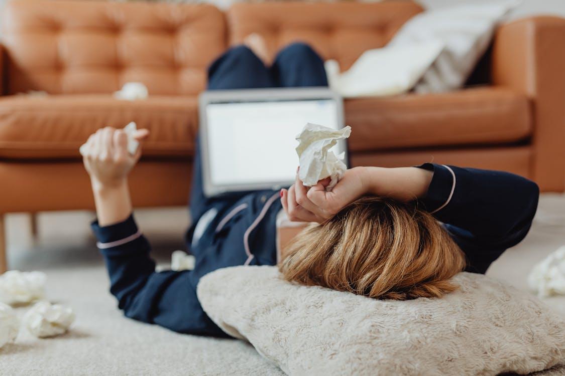 a sick and stressed woman lying on the floor with a laptop in her lap