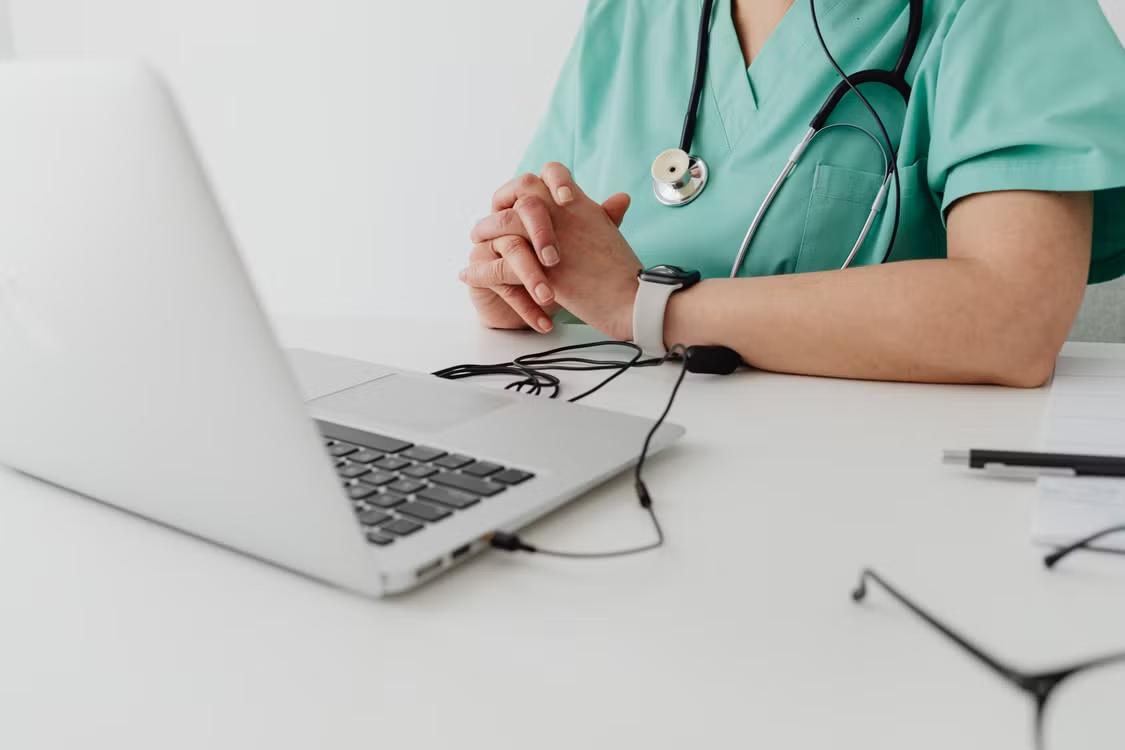 a doctor in a lab coat using a silver laptop.