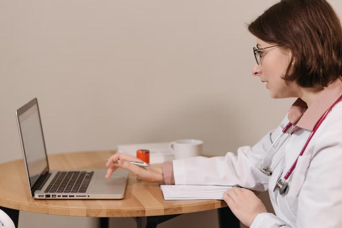 a physician in a white coat using her laptop.