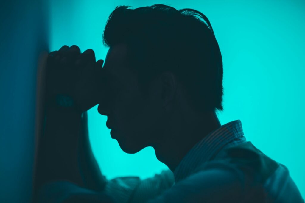 A man holding his head against a wall