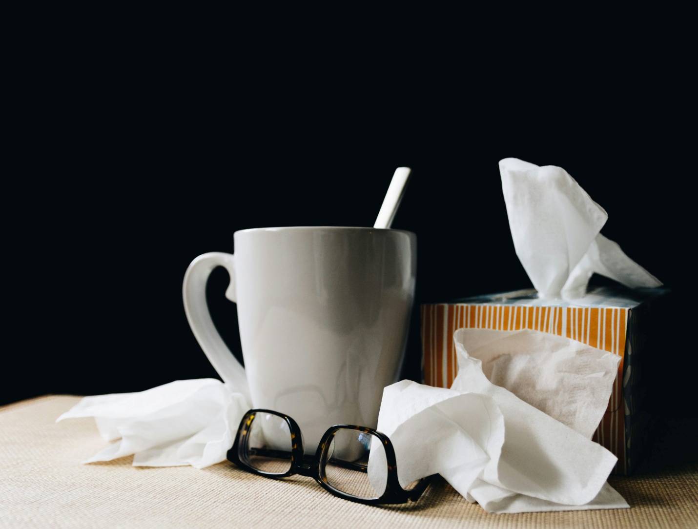 A box of tissues next to a mug and a pair of glasses